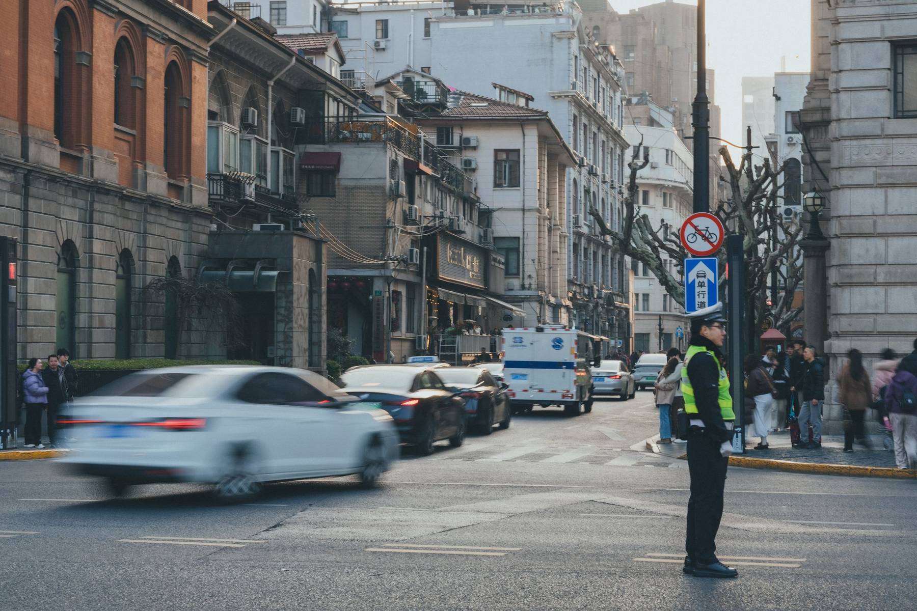 A traffic officer in a high-visibility vest directs cars at a city intersection lined with older buildings